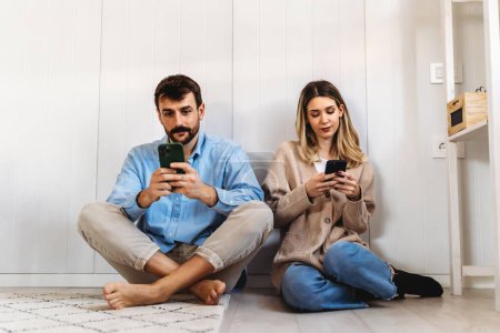 Téléchargez les photos : Couple accro aux smartphones s'ignorant mutuellement à la maison. Problèmes relationnels. Concept de médias sociaux. - en image libre de droit