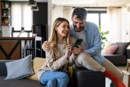 Photo for Smiling young couple embracing while looking at smartphone. Multiethnic couple sharing social media on smart phone. - Royalty Free Image