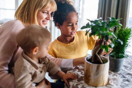 Foto de Mujer joven con sus hijos cuidando plantas en el interior. Familia ocio hogar jardinería hobby concepto. - Imagen libre de derechos