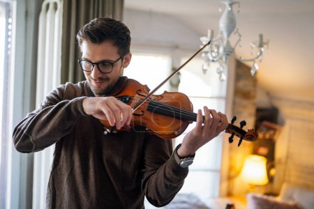 Foto de Un joven guapo caucásico tocando el violín en casa. Hobby calidad tiempo concepto de felicidad. - Imagen libre de derechos