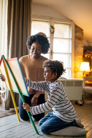 Photo for Happy adorable african american boy enjoying studying with mommys assistance at home. Smiling caring mixed race woman helping for small school aged kid - Royalty Free Image