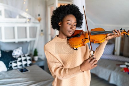 Photo for Young woman learning to play violin at home. Romantic girl playing violin. Portrait of female musician performing on string instrument. Dreamy violinist fingers pressing strings on violin - Royalty Free Image