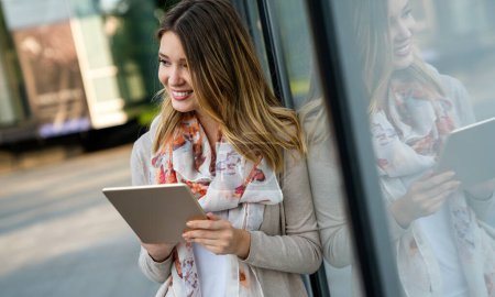 Téléchargez les photos : Jeunesse et technologie. Attrayant jeune femme d'affaires heureuse en utilisant un ordinateur tablette à l'extérieur. - en image libre de droit