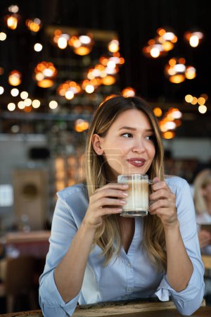 Photo for Portrait of happy young successful business woman drinking coffee in a break. In the background, her colleagues - Royalty Free Image