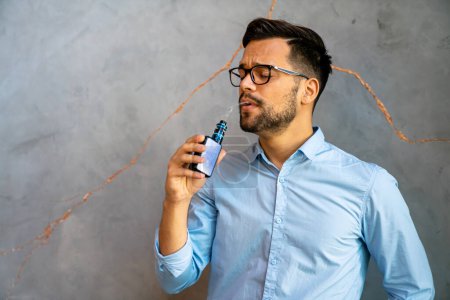 Photo for Smoking and vaping may be unhealthy and addictive and pose health risk to lungs. Man using e-cigarette. - Royalty Free Image