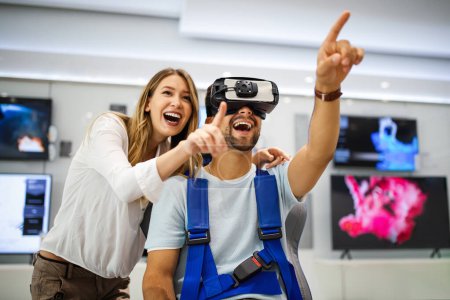 Photo for Young happy couple playing video games with virtual reality glasses in technical store. Cheerful people having fun with new trends technology - Royalty Free Image