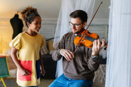 Foto de La música es muy divertida. Padre joven enseñando a su hija a tocar el violín y sonreír. Concepto de felicidad del niño padre. - Imagen libre de derechos