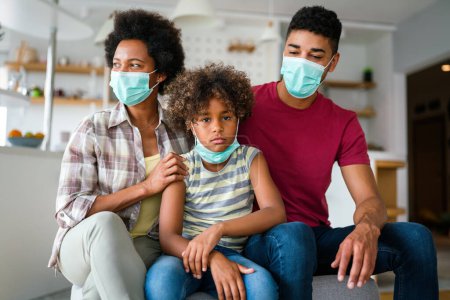 Photo for African american young family in protective medical masks in the midst of the coronavirus pandemic at home - Royalty Free Image
