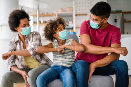 Téléchargez les photos : Jeune famille afro-américaine portant des masques médicaux protecteurs au milieu de la pandémie de coronavirus à la maison - en image libre de droit