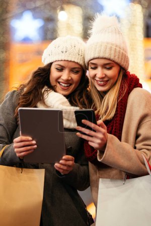 Photo for Happy female friends using digital tablet for online shopping at Christmas in the city. - Royalty Free Image