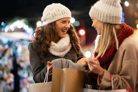 Téléchargez les photos : Les femmes heureuses parlent et rient en plein air en ville à Noël. Bonheur shopping gens vente concept - en image libre de droit