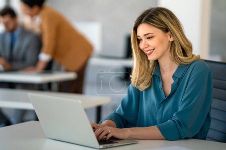 Téléchargez les photos : Jeune femme d'affaires heureuse et prospère travaillant avec un ordinateur portable dans un bureau d'entreprise. Concept de personnes technologiques - en image libre de droit