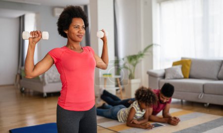 Photo for African american woman with family on background working out at home. Fitness and healthy lifestyle concept. - Royalty Free Image