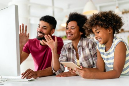 Téléchargez les photos : Heureuse jeune famille afro-américaine s'amuser ensemble tout en utilisant l'ordinateur ensemble à la maison - en image libre de droit