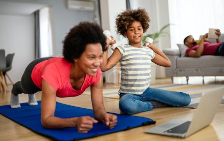 Photo for Beautiful black mother and teen daughter having online yoga class together, making exercises on fitness mat in front of laptop - Royalty Free Image