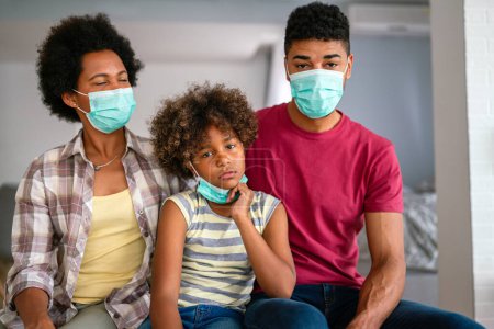 Photo for Young african american family in medical masks during home quarantine. Family is wearing facemasks during coronavirus and flu outbreak. Virus and illness protection, COVID - Royalty Free Image