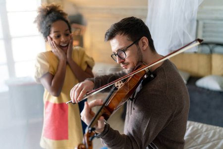 Téléchargez les photos : Père célibataire et fille adoptive jouant de l'instrument ensemble. Homme adulte jouant du violon pour enfant fille. - en image libre de droit