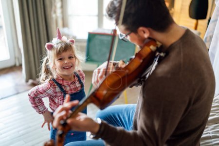 Photo for Happy single father smiling at his daughter while playing a violin at home. Father and daughter spending some quality time. - Royalty Free Image