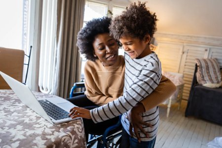 Photo for Young afro american child writing something in notebook with mother while working remotely from home on laptop - Royalty Free Image
