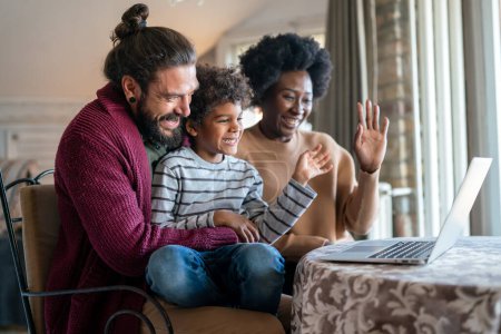 Photo for Happy diverse multiethnic family gathering around laptop and having fun during a video call at home. Multi ethnic parents enjoying quality time with child while using digital device. - Royalty Free Image