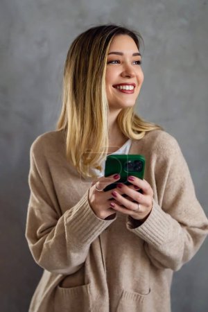 Photo for Young girl wearing sweater using smartphone at home, communication and social network concept, woman browsing the internet - Royalty Free Image