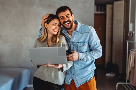 Photo for Portrait of a smiling couple looking at laptop together at cozy home office. People technology fun concept. - Royalty Free Image