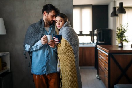 Photo for Cheerful young couple covered in blanket embracing while holding cups of tea at home. Happiness people concept - Royalty Free Image