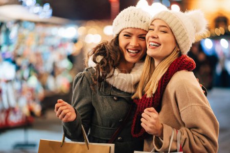 Photo for Cheerful young women friends at christmas time are having fun and buying presents for their family. Xmas, shopping people concept - Royalty Free Image