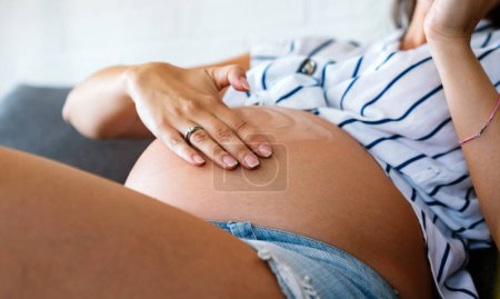 Téléchargez les photos : Grossesse, soins de la peau et concept de maternité. Jeune femme enceinte appliquant la crème vergeture sur le ventre - en image libre de droit