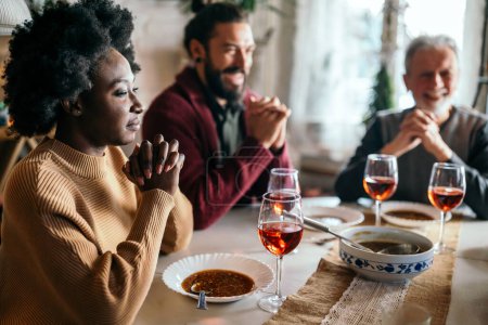 Téléchargez les photos : Heureuse famille multiethnique priant avant le repas à la maison. Concept de religion populaire - en image libre de droit