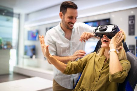 Téléchargez les photos : Jeune couple heureux jouant à des jeux vidéo avec des lunettes de réalité virtuelle en magasin technique. Des gens joyeux qui s'amusent avec les nouvelles technologies de tendances - en image libre de droit