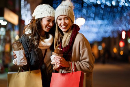 Téléchargez les photos : Portrait de femmes heureuses profitant de la foire de Noël et faisant du shopping ensemble à l'extérieur. vacances gens bonheur concept - en image libre de droit