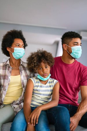 Photo for Young african american family in medical masks during home quarantine. Family is wearing facemasks during coronavirus and flu outbreak. Virus and illness protection, COVID - Royalty Free Image