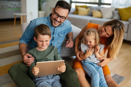 Téléchargez les photos : Joyeux jeune famille s'amuser à la maison. Parents avec enfants utilisant une tablette. Les gens aiment le concept de bonheur. - en image libre de droit