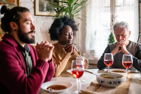 Téléchargez les photos : Heureuse famille multiethnique priant avant le repas à la maison. Concept de religion populaire - en image libre de droit