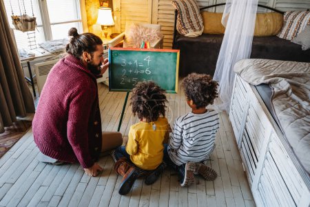 Téléchargez les photos : Enfants heureux d'apprendre les mathématiques avec un père adoptif diversifié, enseignant à la maison. Éducation familiale concept bonheur - en image libre de droit
