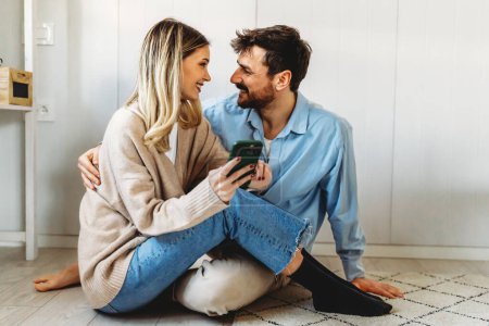 Foto de Sonriendo joven pareja abrazando mientras mira el teléfono inteligente. Pareja multiétnica compartiendo redes sociales en el teléfono inteligente. - Imagen libre de derechos
