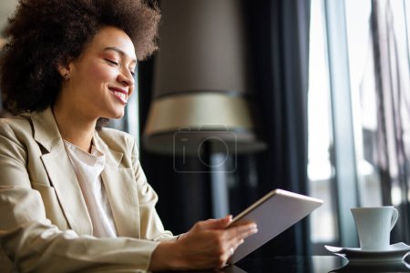 Photo for Young modern successful african american business woman working using digital tablet while sitting in the office - Royalty Free Image