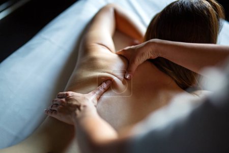Foto de Feliz masajista profesional que masajea detrás de una joven cliente relajada en la mesa de masaje en el salón de spa - Imagen libre de derechos