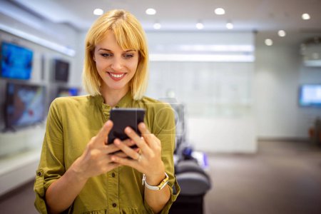 Téléchargez les photos : Femme heureuse vérifiant les médias sociaux tenant un téléphone intelligent. Sourire jeune femme en utilisant l'application de téléphone mobile jeu, achats en ligne, commande de livraison - en image libre de droit