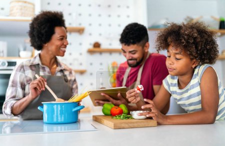 Téléchargez les photos : Heureuse famille afro-américaine souriante préparant des aliments sains dans la cuisine, s'amusant ensemble le week-end - en image libre de droit