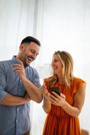 Téléchargez les photos : Jeune couple souriant embrassant tout en utilisant un smartphone. Personnes partageant les médias sociaux sur un téléphone mobile. - en image libre de droit