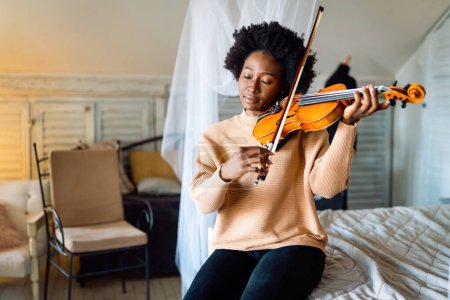 Téléchargez les photos : Jolie jeune musicienne noire joue du violon pratiquant l'instrument de musique à la maison - en image libre de droit