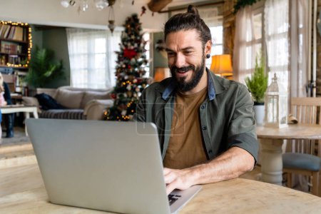 Téléchargez les photos : Jeune homme hipster heureux beau utilisant un ordinateur portable à la maison. Personnes technologie en ligne Internet dispositif numérique concept - en image libre de droit