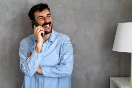 Téléchargez les photos : Heureux homme caucasien riant pendant la conversation smartphone. Communiquer via un gadget de téléphone portable, l'homme en utilisant l'application - en image libre de droit