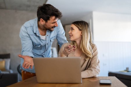 Téléchargez les photos : Joyeux jeune couple utilisant un ordinateur portable et souriant tout en faisant du shopping en ligne à la maison ensemble - en image libre de droit