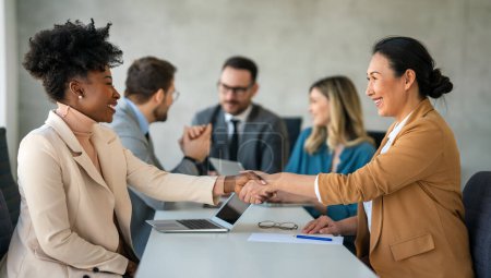 Photo for Business shaking hands, finishing up meeting. Successful multiethnic businesswomen handshaking after good deal. - Royalty Free Image