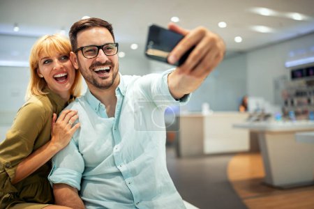 Foto de Hermosa pareja joven está abrazando, haciendo una selfie usando un teléfono inteligente y sonriendo. Dispositivo digital, concepto de inteligencia artificial. - Imagen libre de derechos