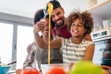 Foto de Feliz afroamericana sonriente familia preparando comida saludable en la cocina, divirtiéndose juntos el fin de semana - Imagen libre de derechos