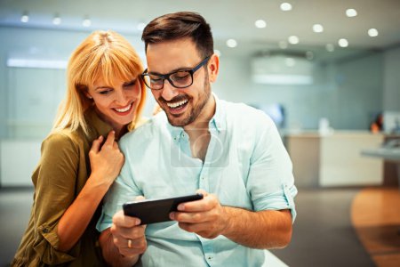 Photo for Smiling young couple have fun using smartphone together, happy caucasian man and woman watch video on cellphone, make self-portrait picture on cell - Royalty Free Image